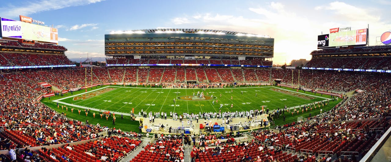 Home A stunning panoramic shot of Levi's Stadium in Santa Clara during a packed football game at sunset.